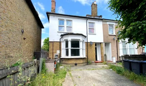Semi-detached house with white and brick facade, bay window, and paved front yard.