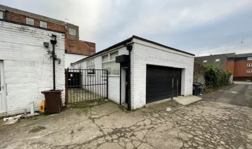 White brick industrial unit with black roller door and gated yard.