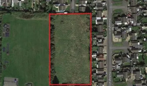 Aerial view of vacant land outlined in red, next to residential houses and a park.