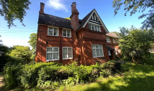 Red brick house with white-trimmed windows, black and white gabled roof, and surrounding greenery.