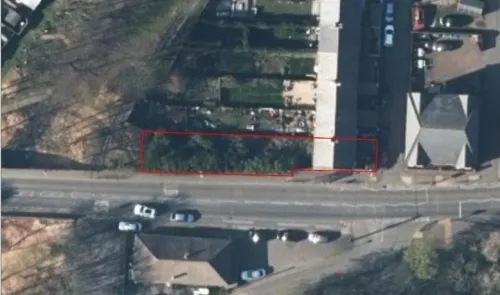 Aerial view of overgrown land (outlined in red) next to a road and buildings.