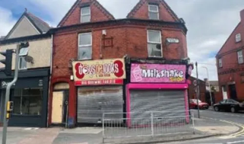 Red brick retail building with "Tops & Looks" and "Milkshake Shop" signage, metal security gates down.