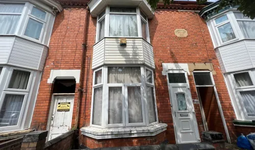 Red brick terraced house with bay window, "Lambourne Villas 1900" plaque, and CCTV warning sign.