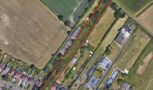Aerial view of a narrow, red-outlined land parcel amidst fields and buildings.