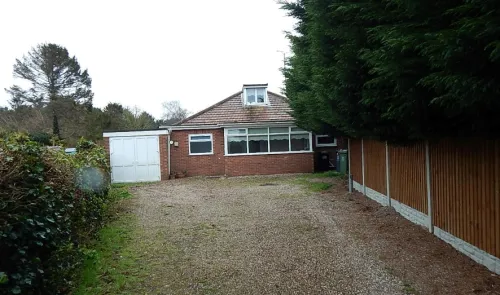 Red brick bungalow with attached garage, gravel driveway, and wooden fence.