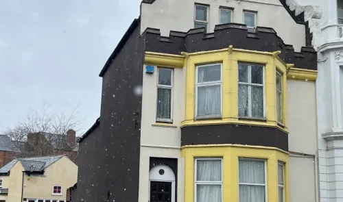 Yellow and dark grey house exterior with bay windows, light snow falling.