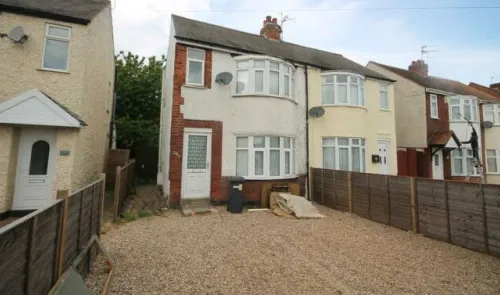 Semi-detached house with bay windows, gravel driveway, and wooden fence.