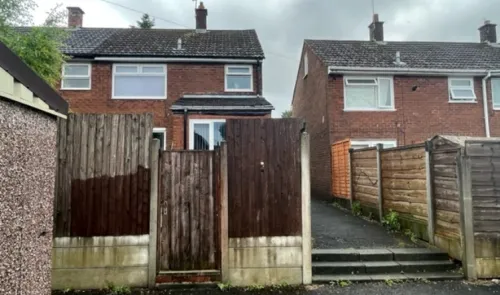 Rear view of a brick house with a gated wooden fence and driveway.