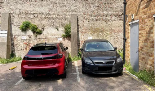 Two cars parked in an off-street parking lot by a brick wall.
