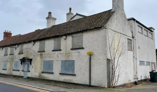 Boarded-up white two-story building with multiple chimneys and tiled roof.
