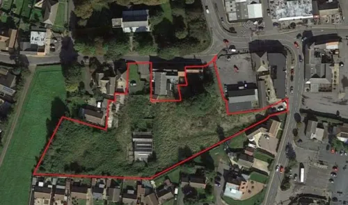Aerial view of land outlined in red, showing buildings, vegetation, and adjacent roads.