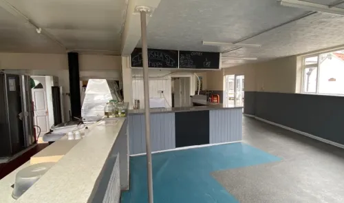 Empty cafe interior with serving counter, chalkboard menu, and blue and grey flooring.