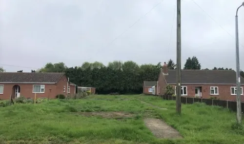 Overgrown grassy area between two brick bungalows.