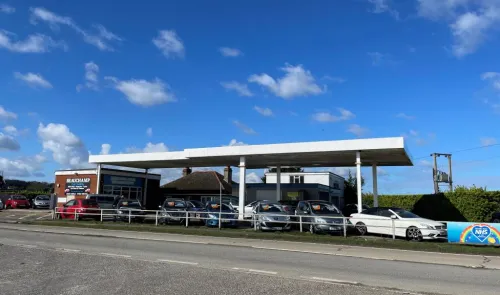 Beauchamp Car Sales forecourt displaying used cars for sale under a petrol station canopy.