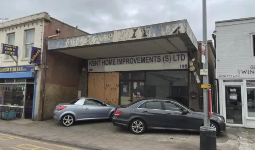 Kent Home Improvements (S) LTD storefront with boarded-up windows, parked cars, and adjacent businesses.