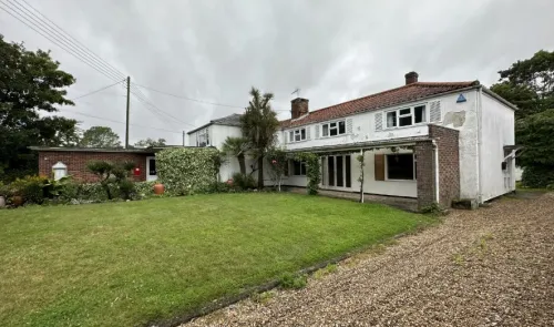 White detached house with red tiled roof, covered porch, and gravel driveway, viewed from the front garden.