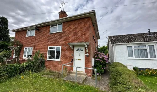 Red brick house exterior with white door, access ramp, and front garden.