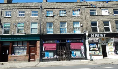 Brick storefronts with "Bycroft" real estate office and "M Print" shop on sunny street.