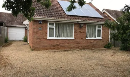 Red brick bungalow with solar panels, white windows, and gravel driveway.