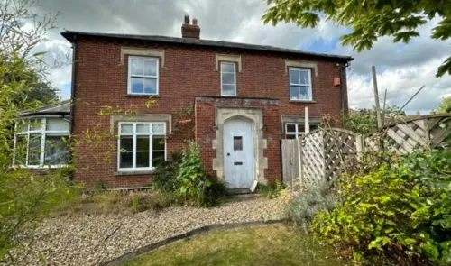 Red brick house with white arched doorway and overgrown front garden.