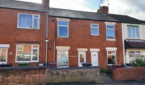 Red brick terraced house with white doors and windows, seen on a sunny day.