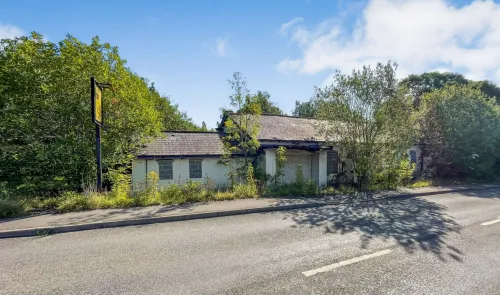 Derelict roadside building with boarded windows, overgrown vegetation, and faded signage.