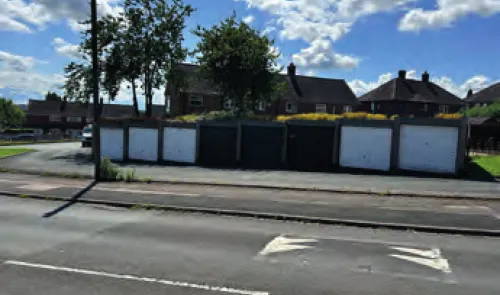 Row of garages behind houses, seen from across the road.