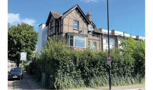 Tudor-style house with bay window behind a tall hedge. Road works sign visible.