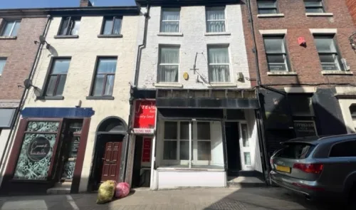 White and brick multi-story commercial building with empty storefront.