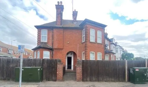 Red brick house with two chimneys behind a wooden fence.