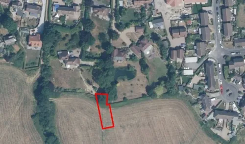 Aerial view of land plot outlined in red, adjacent to residential properties and fields.