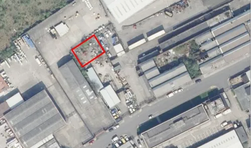 Aerial view of a commercial property site with a red-outlined area, surrounded by industrial buildings and parking lots.