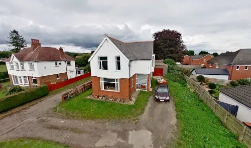 White and brick detached house with front garden and driveway, viewed from above.