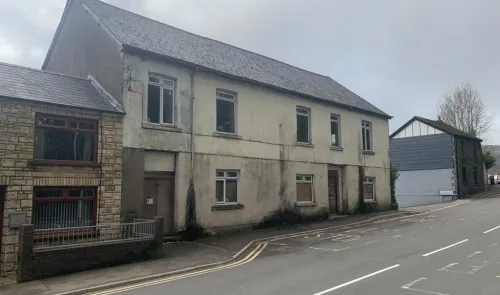 Two-story property with boarded windows and slate roof, needs renovation.
