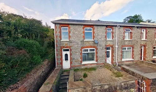 Stone terraced house with red brick accents, white windows, and front garden.
