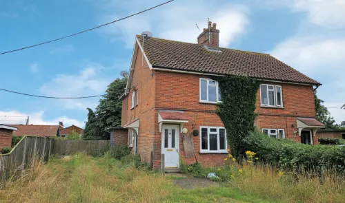 Red brick two-story house with overgrown front yard.
