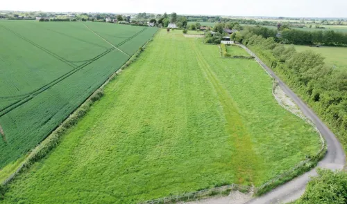 Aerial view of a lush green field bordered by a road and farmland.