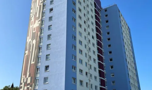 Modern high-rise apartment building with blue, white, and maroon facade and large abstract mural.