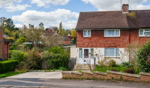 Red brick house with front garden and driveway, village church in background.