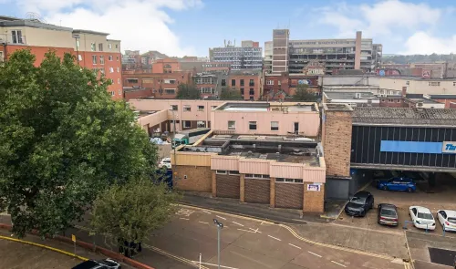 Elevated view of a commercial property with flat roof, street, parked cars, and city buildings in the background.