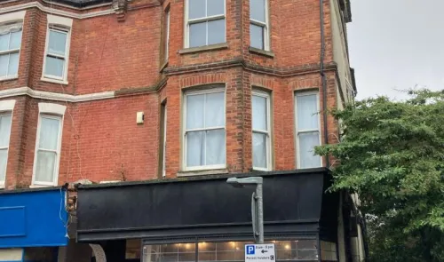 Red brick building with multiple windows above a shop front. Parking sign visible.