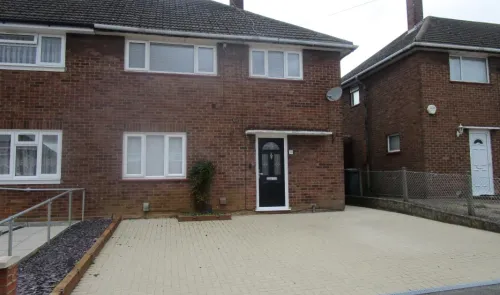 Red brick house with white windows, black front door, and paved driveway.
