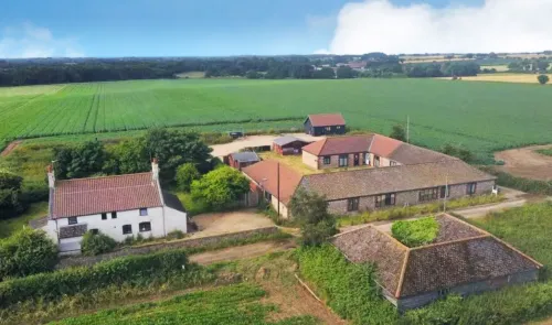 Aerial view of a farmhouse, outbuildings, and surrounding green fields.