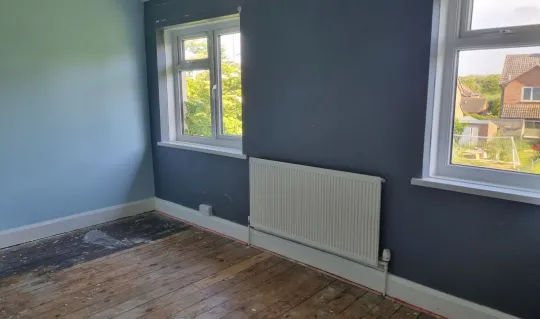 interior of bedroom with slate grey blue coloured walls, wall mounted radiator and exposed floorboards