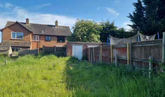 overgrown back garden with exterior of brown brick house at the end